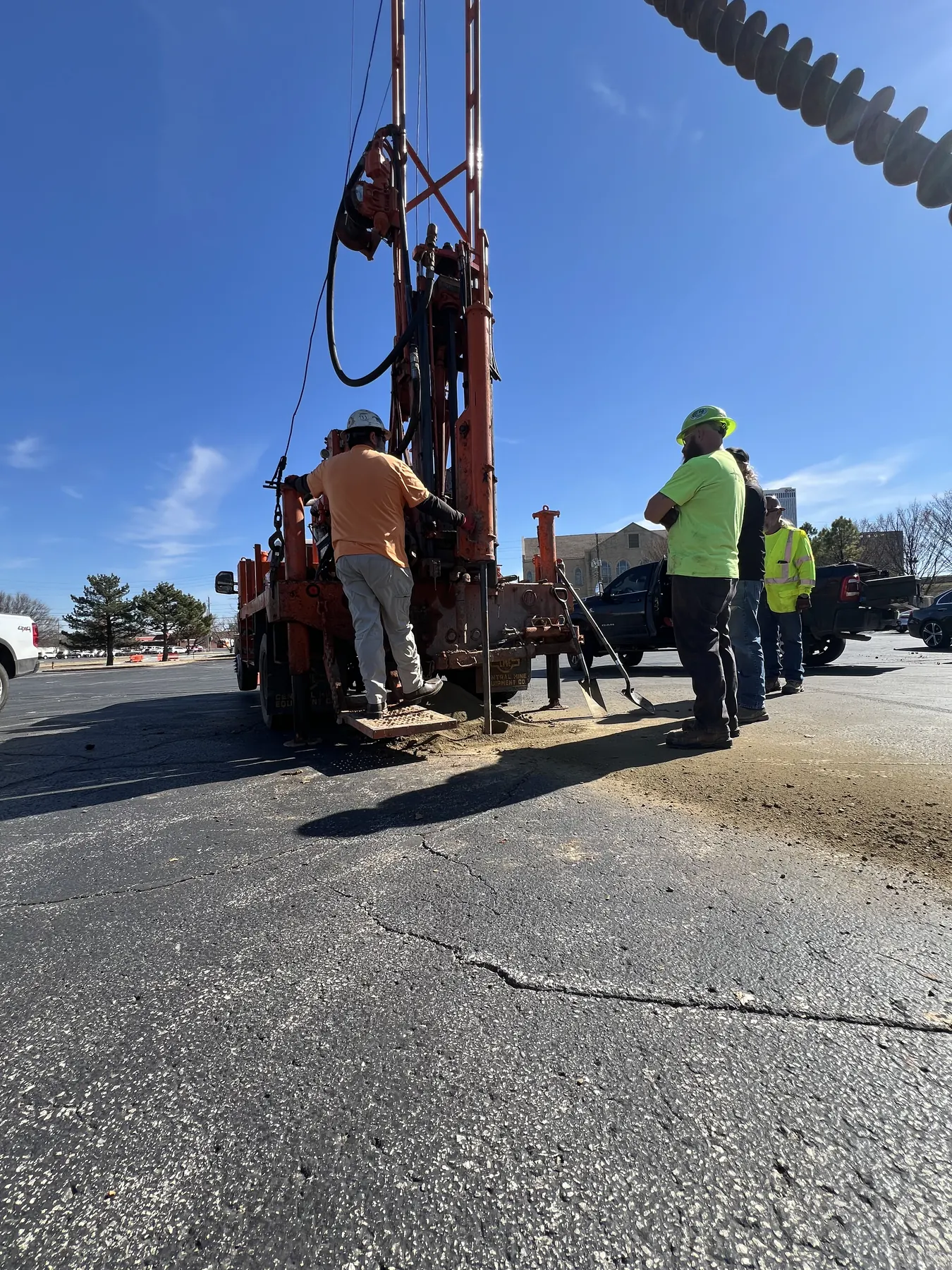Field technicians operating an orange truck-mounted drilling rig beneath a clear blue sky