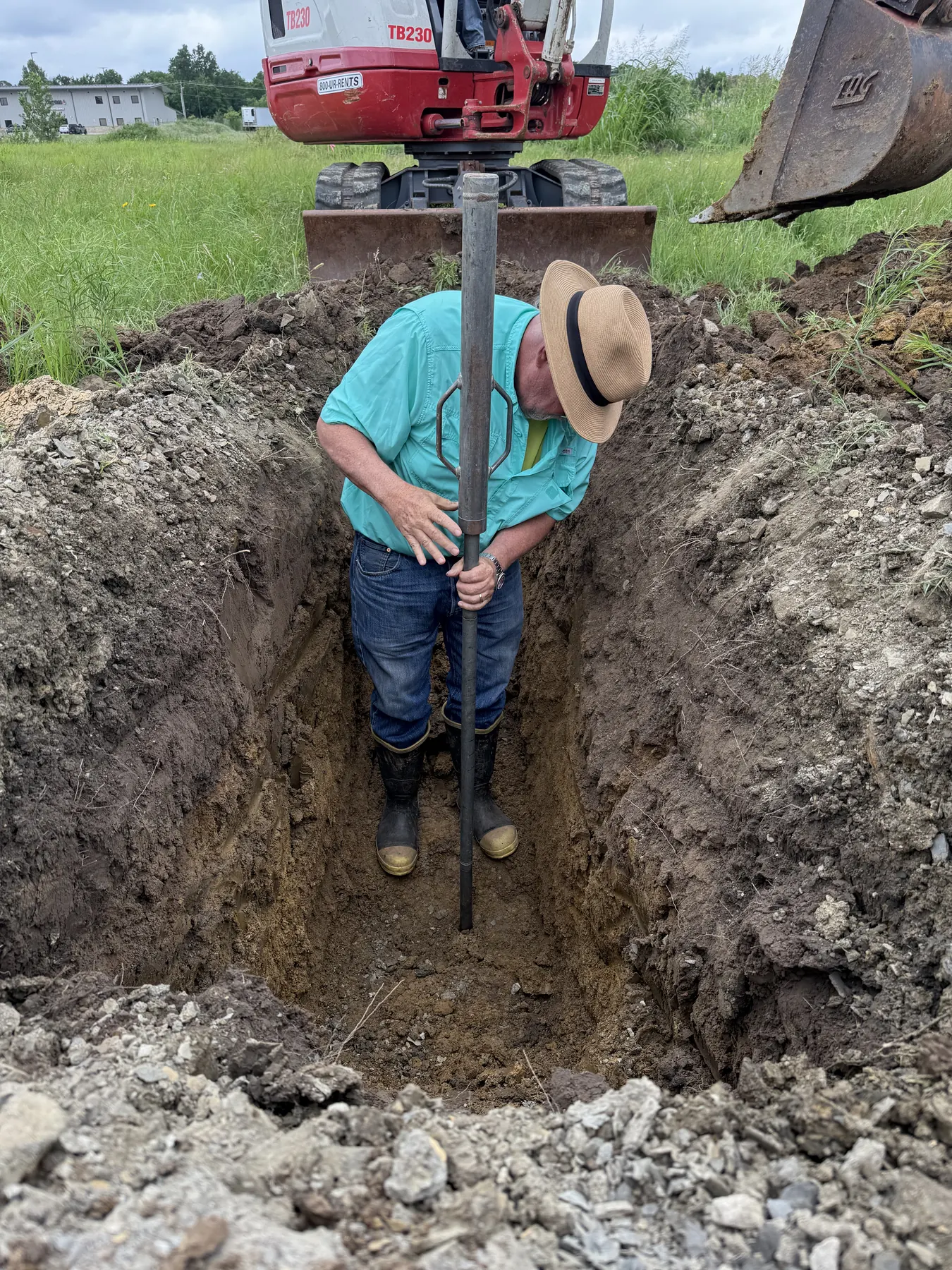 A field technician takes a measurement at the bottom of a freshly excavated test pit
