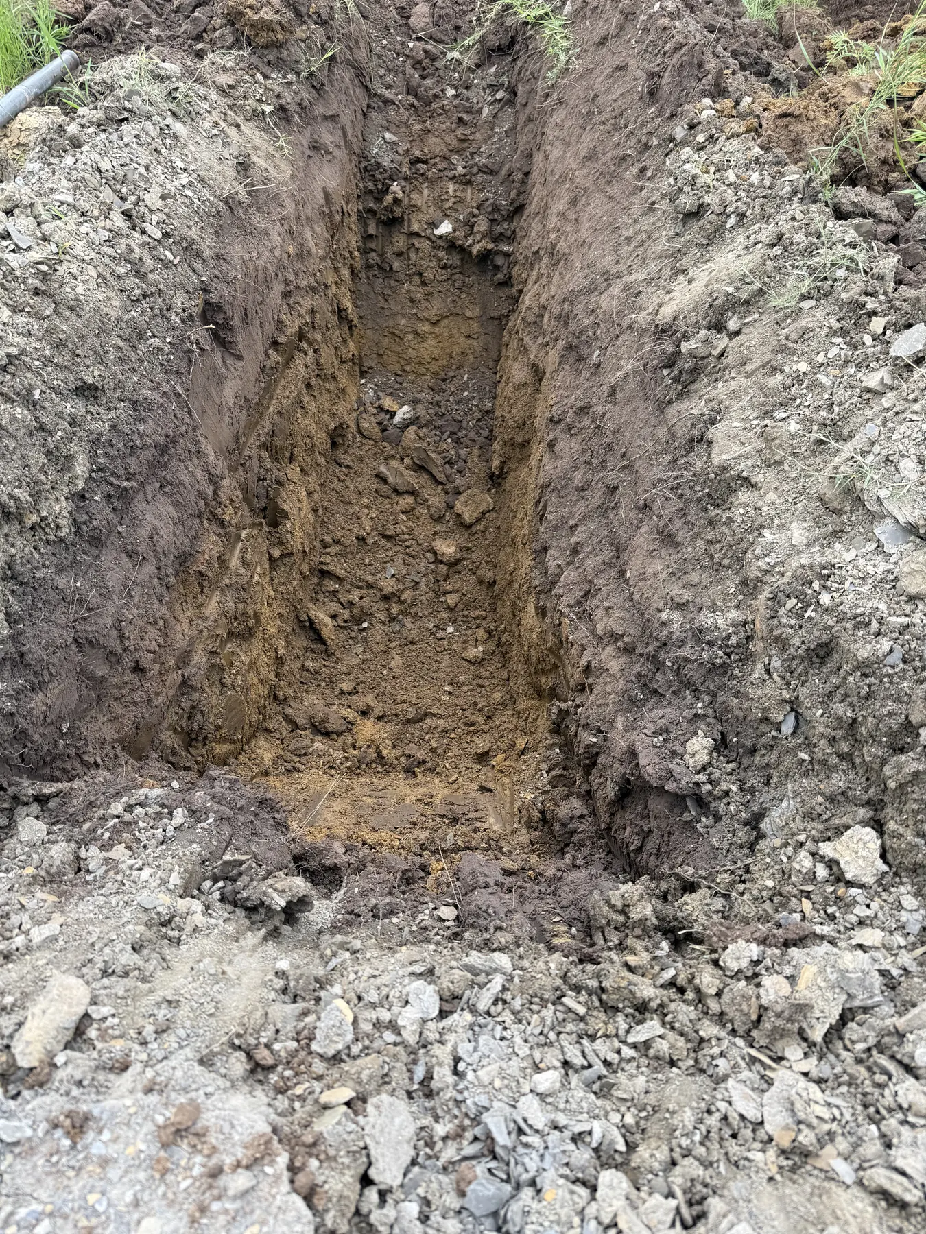 A deep open test pit with rough soil walls and a gravelly excavation floor